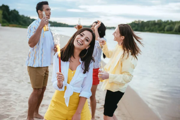 Jovem Alegre Segurando Sparkler Olhando Para Câmera Enquanto Diverte Praia — Fotografia de Stock