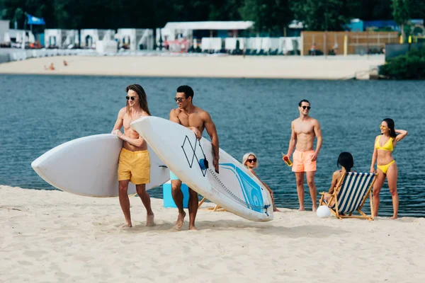 Handsome Young Multicultural Men Holding Surfing Boards While Walking Beach — Stock Photo, Image