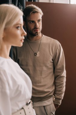 selective focus of attractive blonde girl and bearded young man with hand in pocket on brown clipart