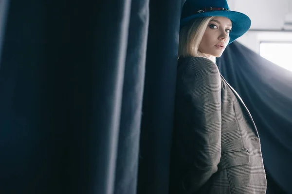 カーテンの近くに立っている帽子とジャケットのスタイリッシュなブロンドの女の子 — ストック写真