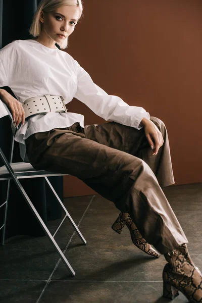 Stijlvolle Blonde Vrouw Witte Blouse Laarzen Met Slangenhuid Print Zittend — Stockfoto