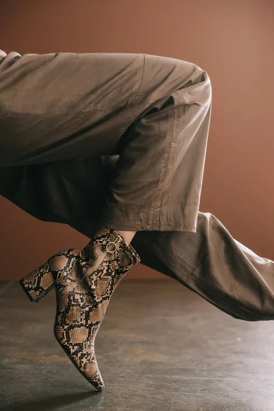 partial view of woman in pants and boot with snakeskin print on brown