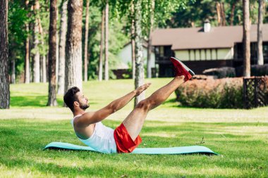 sakallı atletik sporcu nun yan görünümü dışında fitness mat üzerinde çalışıyor 