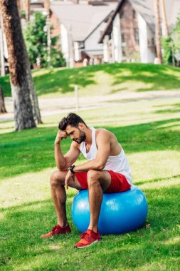 parkta mavi fitness topu üzerinde oturan üzgün sporcu 
