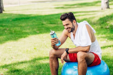 fitness topu otururken spor şişesi bakarak mutlu sakallı adam 