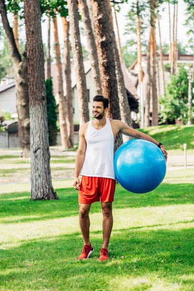 緑の草の上に立って 青いフィットネスボールを保持している陽気なスポーツマン — ストック写真