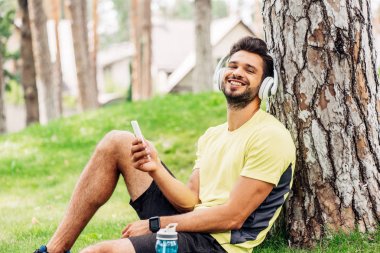 kulaklık mutlu adam ağacın yanında oturan ve akıllı telefon tutarak 