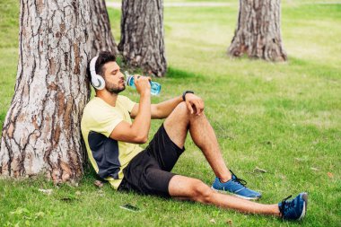 kulaklıklı sakallı sporcu ağaç gövdesi yakınında su içme 