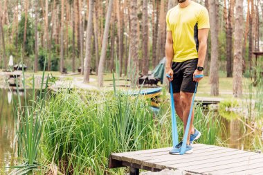 cropped view of sportsman working out with suspension straps near lake  clipart