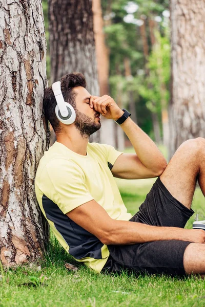 Sportsman Headphones Covering Face While Holding Sport Bottle Tree Trunk — Stock Photo, Image