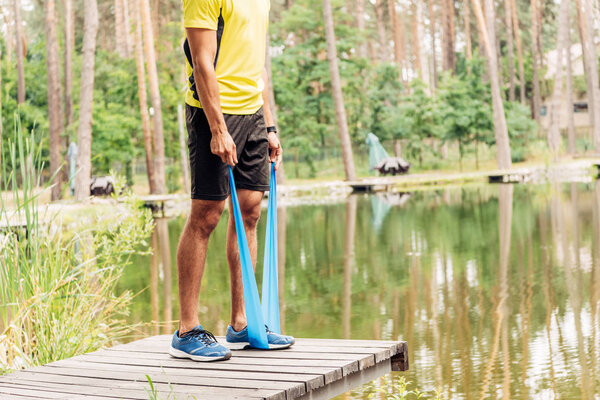 cropped view of man exercising with suspension straps near lake 