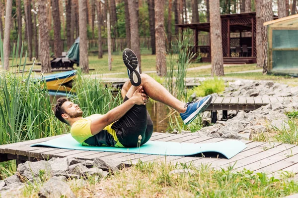 英俊的运动员在森林附近的树木和石头附近的健身垫上锻炼 — 图库照片