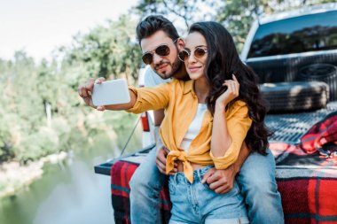 araba ve göl yakınında sakallı adam ile selfie konuşurken güneş gözlüğü neşeli kız