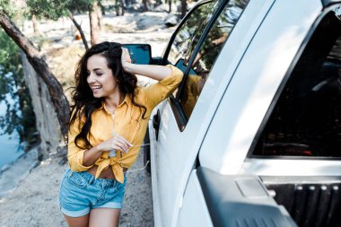 ormanda arabanın yanında dururken gülümseyen mutlu kadının seçici odak 