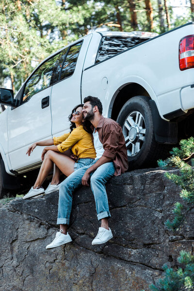 happy bearded man and attractive girl sitting near car in woods 