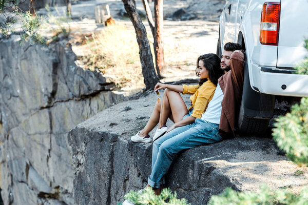 selective focus of handsome man and attractive girl sitting near car 