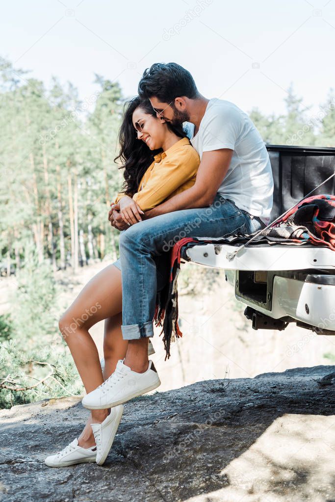 bearded man hugging attractive girl in sunglasses near automobile 