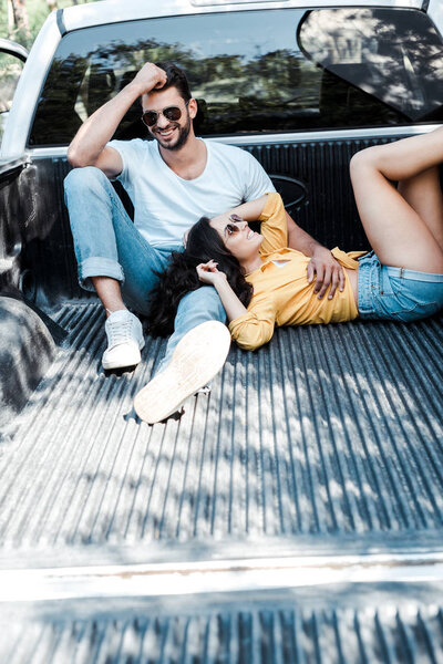 happy man in sunglasses sitting in car trunk near girl 
