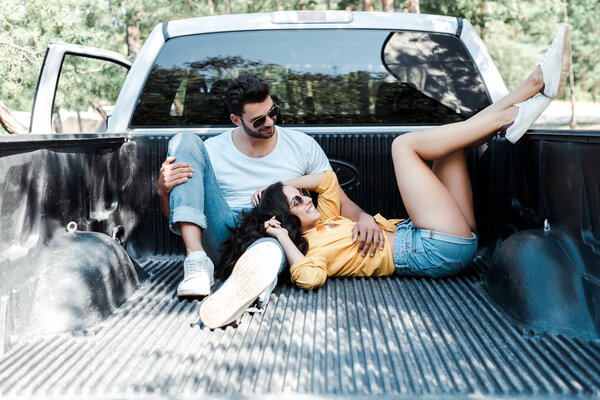 cheerful man in sunglasses sitting in car trunk near girl 
