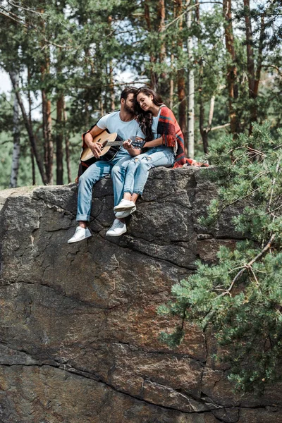 森の中で魅力的な女性の近くでアコースティックギターを演奏するひげを生やした男 — ストック写真
