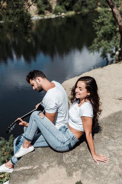 overhead view of man playing acoustic guitar near woman and lake 