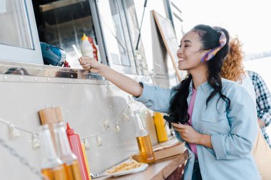 selective focus of happy asian girl holding credit card near customers and food truck  clipart