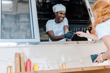 low angle view of redhead girl giving cash to happy african american man in food truck  clipart