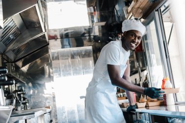 yemek kamyonunda karton plaka tutarken gülümseyen neşeli Afrikalı Amerikalı şef seçici odak 