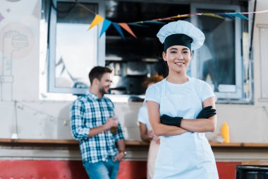 yemek kamyonu ve müşterilerinin yanında çapraz kolları ile ayakta neşeli Asya şef seçici odak 