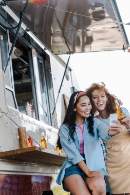 yemek kamyonu yakınında selfie çeken neşeli çok kültürlü kızların seçici odak