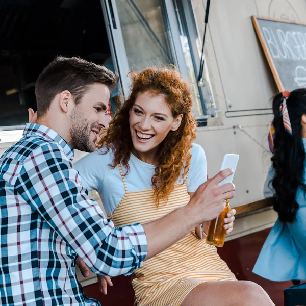 选择性的焦点红发女人看男人拿着智能手机附近的食品卡车 — 图库照片