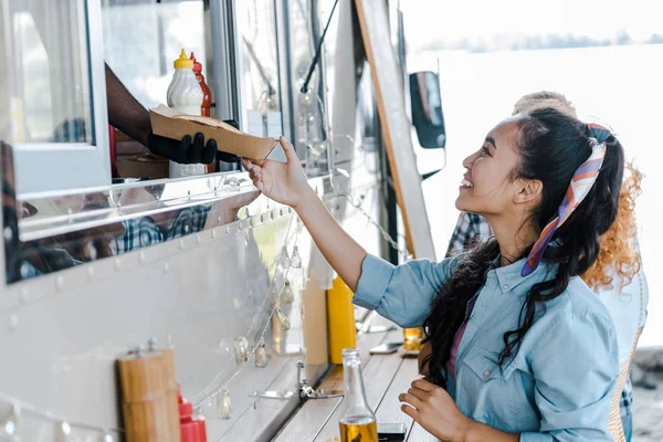 cropped view of african american man giving carton plate to asian girl near food truck