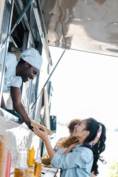 Веселый Африканский Американец Дает Картонную Тарелку Азиатской Девушке Рядом Клиентами — стоковое фото