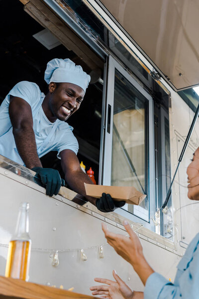 low angle view of happy african american man giving carton plate to asian customer 