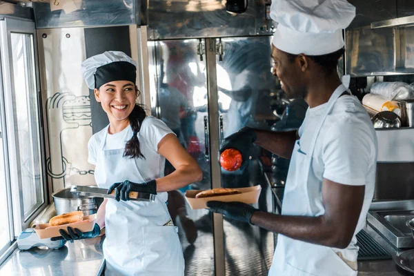 selective focus of happy multicultural chefs holding carton plates with street food