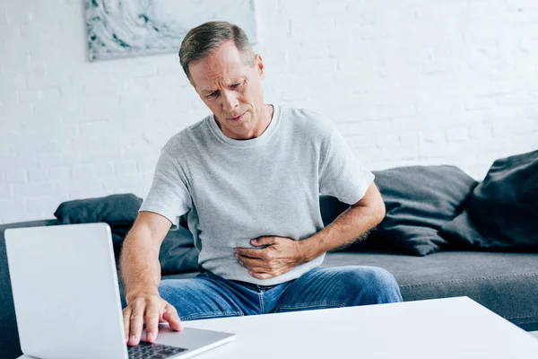 Όμορφος Άντρας Μπλουζάκι Στομαχόπονο Χρησιμοποιώντας Φορητό Υπολογιστή Στο Διαμέρισμα — Φωτογραφία Αρχείου