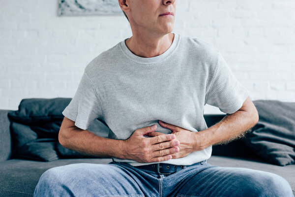 cropped view of man in t-shirt with stomachache in apartment 
