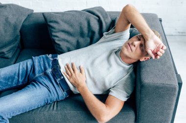 handsome man in t-shirt with stomachache lying on sofa  clipart