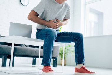 cropped view of man in t-shirt with stomachache in apartment  clipart