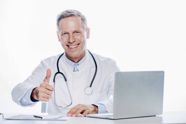 beyaz ceketli yakışıklı doktor gülümseyerek ve başparmak kadar beyaz izole gösteren 