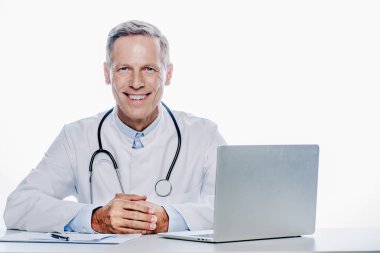 beyaz ceketli yakışıklı doktor gülümseyerek ve beyaz izole kamera bakıyor