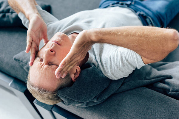high angle view of handsome man in t-shirt with closed eyes touching head in apartment 