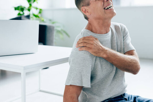 cropped view of handsome man in t-shirt feeling pain in shoulder in apartment 