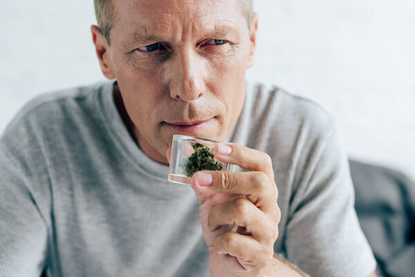 красивый мужчина в футболке, нюхающий медицинскую марихуану в квартире
 