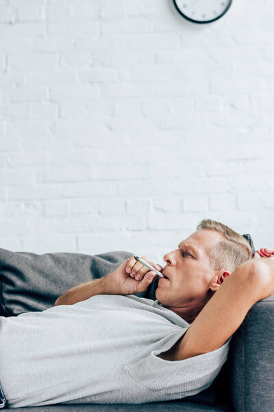 Вид сбоку красивого человека, курящего в квартире морковку с медицинской марихуаной
 