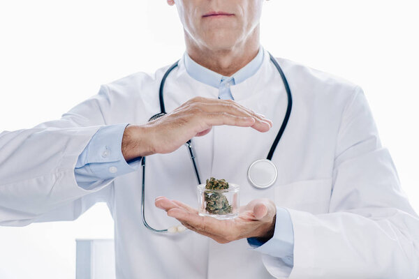 cropped view of doctor in white coat holding medical marijuana isolated on white