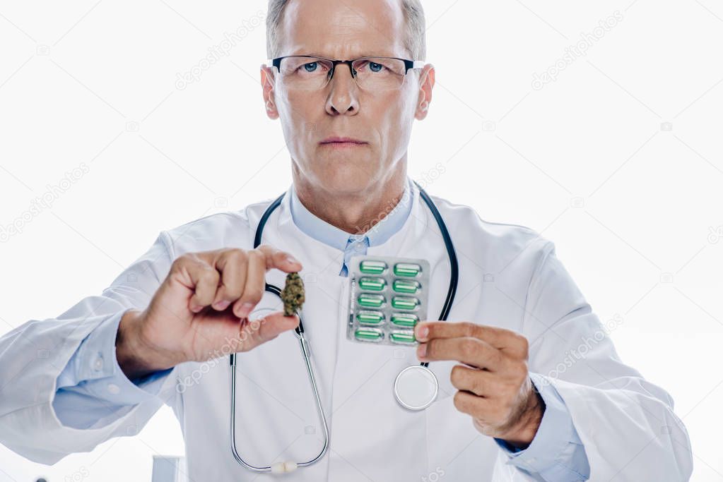 handsome doctor in white coat holding medical marijuana and pills isolated on white
