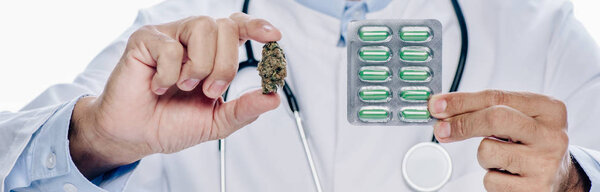 panoramic shot of doctor in white coat holding medical cannabis and pills isolated on white 
