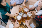 Teilansicht multikultureller Freunde, die Krüge mit hellem und dunklem Bier klappern  