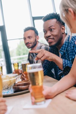 pub çok kültürlü arkadaşlar la otururken parmak ile işaret neşeli afrikalı amerikalı adam seçici odak